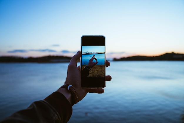 海の背景の画面にokサインと携帯電話を持っている男性の手のクローズアップショット