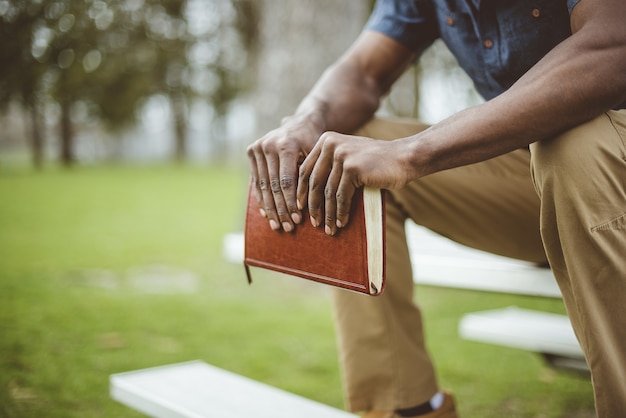 Closeup shot of a male holding the bible while sitting on a park table