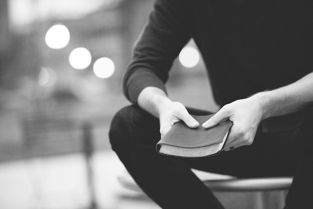 Closeup shot of a male holding the bible with a blurred background in black and white