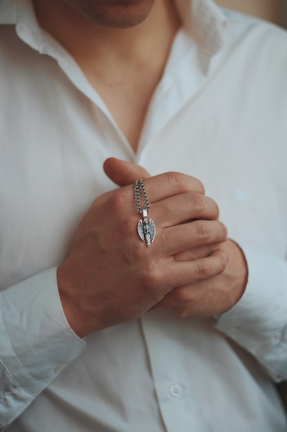 Closeup shot of a male wearing a white shirt holding a silver men's necklace