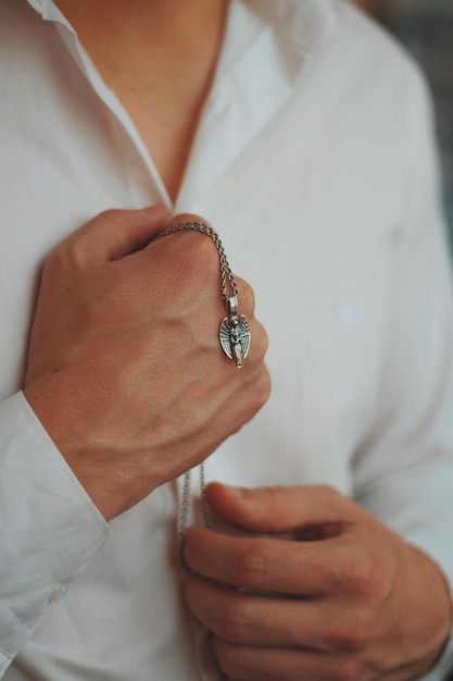 Closeup shot of a male wearing a white shirt holding a silver men's necklace