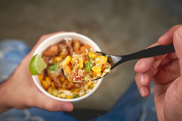 Closeup shot of a man's hand holding a spoonful of salad with corn over a paper bowl