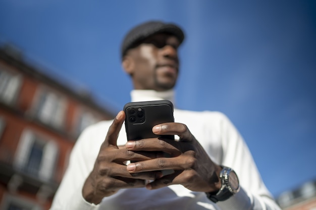 Closeup shot of a man wearing a turtleneck and a hat holding his phone