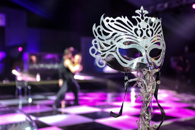 Closeup shot of a mask with a couple dancing in the background