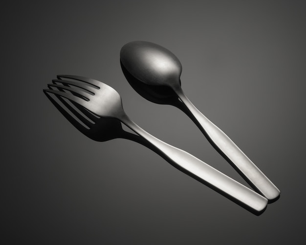 Closeup shot of a metal fork and a spoon isolated on a gray table