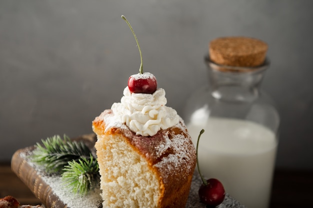 Closeup shot of milk, a delicious cake with cream, powdered sugar, and cherries on books