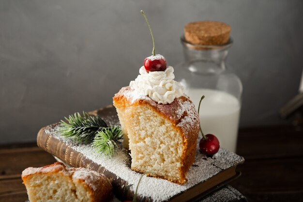 Closeup shot of milk, a delicious cake with cream, powdered sugar, and cherries on books