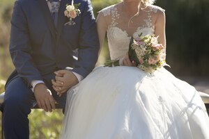 closeup shot of a newlywed couple sitting on a bench while holding hands with each other