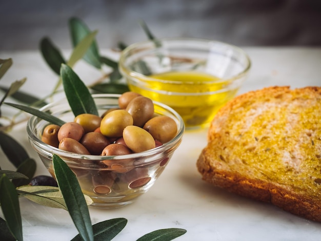 Бесплатное фото Снимок крупным планом кусочков хлеба с маслом первого отжима возле стеклянных мисок, наполненных маслом и оливками