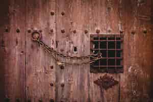 Foto gratuita il colpo del primo piano di vecchia catena arrugginita fissa una grande porta di legno con un piccolo recinto del metallo