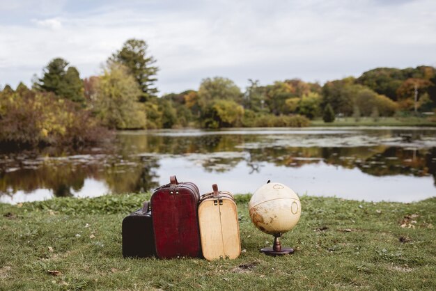Closeup shot of old suitcases on a grassy field near desk globe with blurred water