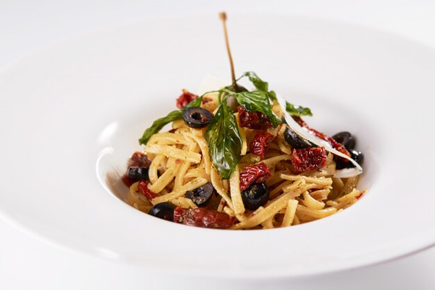 Closeup shot of pasta with dried fruits, olives, and mint on a white wall