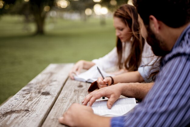 Closeup shot of people sitting in the park and reading the Bible