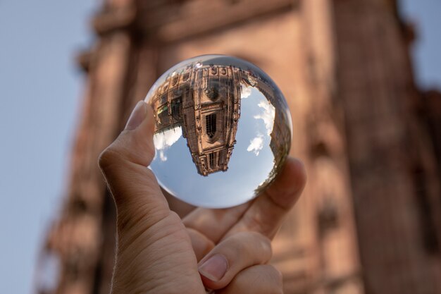 Closeup shot of a person holding a crystal ball with the reflection of historic buildings