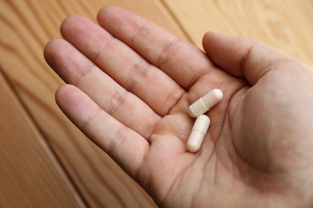 Closeup shot of a person holding two capsules on the palm of his hand