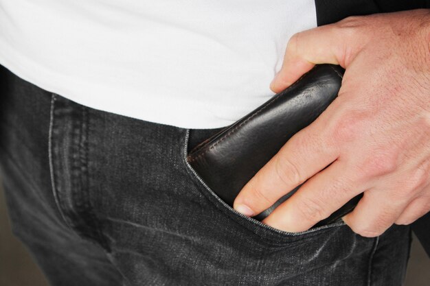 Снимок крупным планом человека, кладущего кожаный бумажник в карман