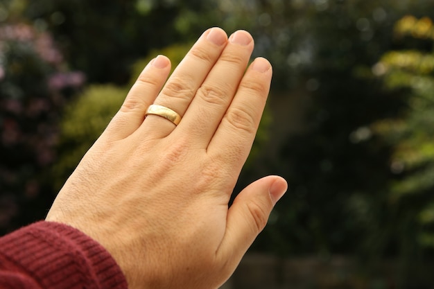 Closeup shot of a person's hand wearing a golden wedding ring with a blurred natural