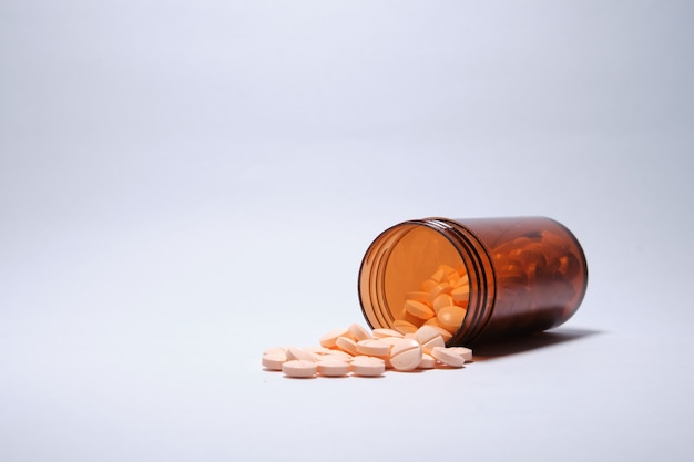 Closeup shot of pink tablets fallen out brown bottle on white surface