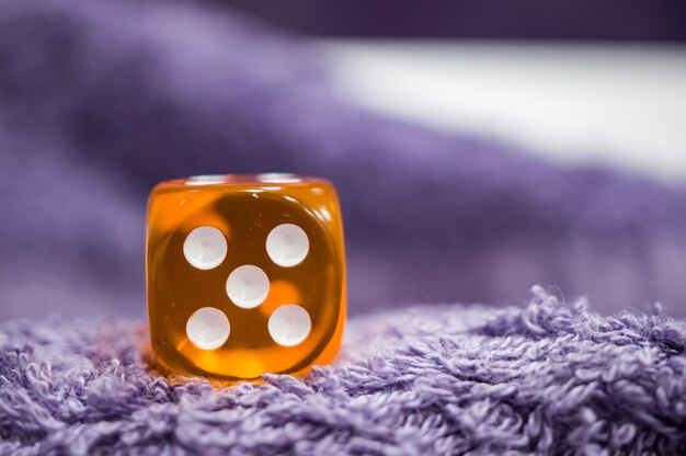 Closeup shot of a plastic orange dice with five dots  on a soft fabric