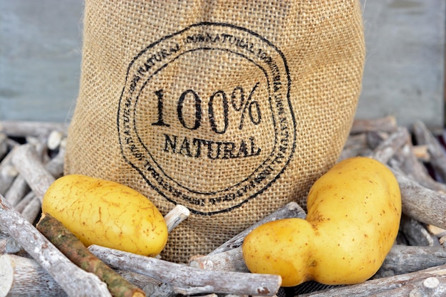 Free photo closeup shot of potatoes and twigs next to a burlap sack in front of a wooden surface