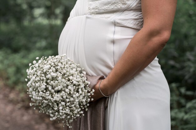 Closeup shot of a pregnant bride holding a white bouquet on her wedding day