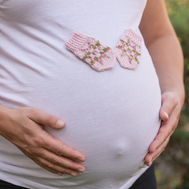 Closeup shot of a pregnant female with a pair of cute baby mittens on her belly