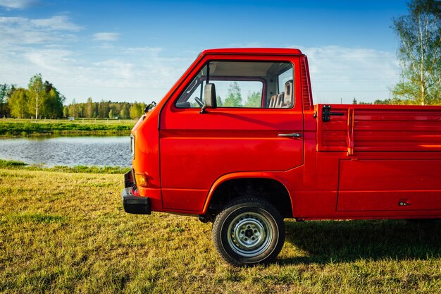 Closeup shot of a red truck on the green field next to the water