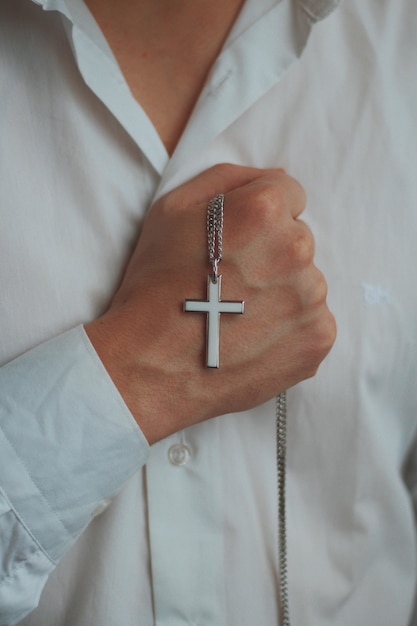 Снимок крупным планом религиозного мужчины, держащего серебряное ожерелье с крестом