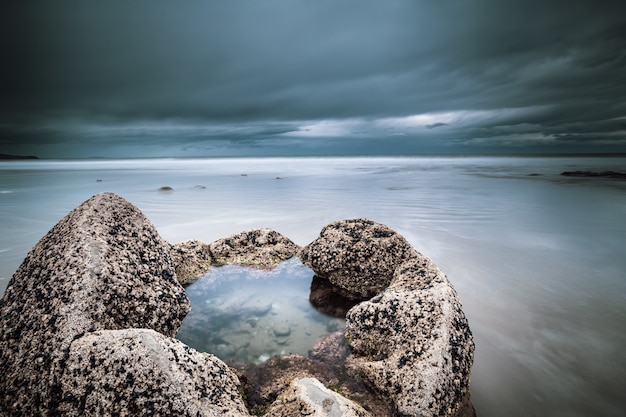 Closeup shot of rock filled with in the middle in the sea under a blue cloudy sky