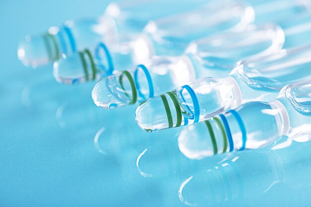 Closeup shot of a row of closed glass vials with clear liquid on a blue surface