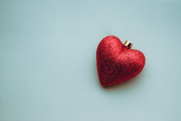 Closeup shot of shiny heart-shaped Christmas tree decoration on a light blue surface