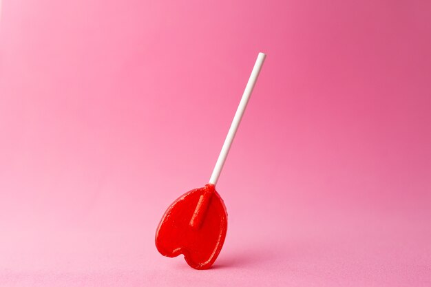 Closeup shot of a single heart-shaped lollipop on a pink background