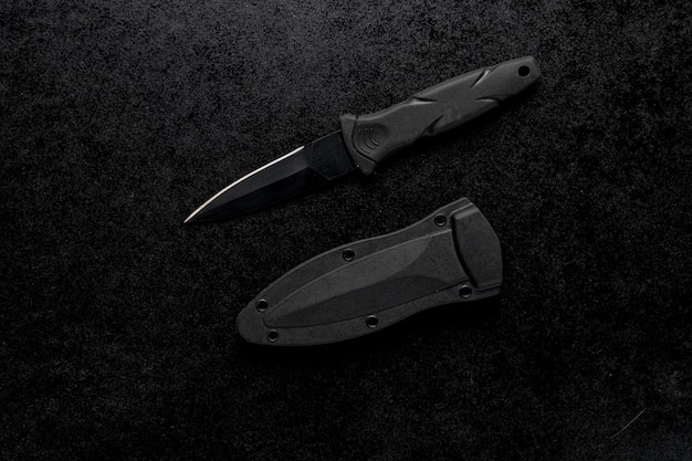 Closeup shot of a small sharp army knife with a black handle on a black table