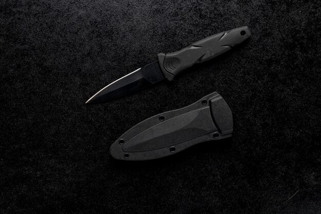 Closeup shot of a small sharp army knife with a black handle on a black table