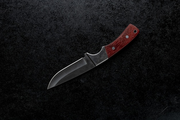 Closeup shot of a small sharp knife with a brown handle on a black background