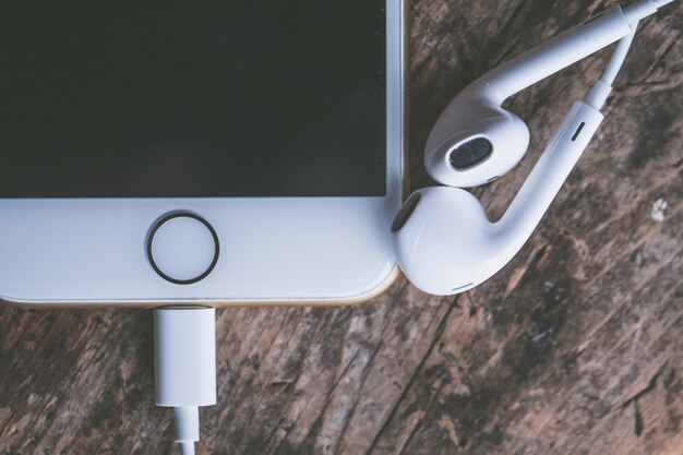 Closeup shot of a smartphone with connected headphones on a wooden surface