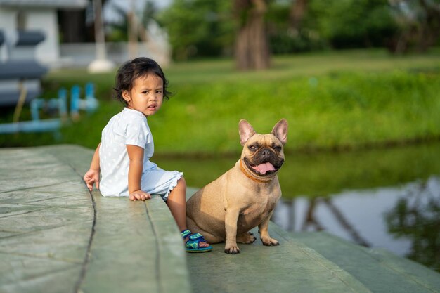 Closeup shot of a Southeast Asian kid with a French bulldog outdoors