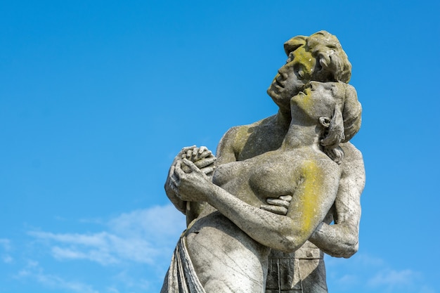 A closeup shot of a stone made a statue of a couple with a blue sky