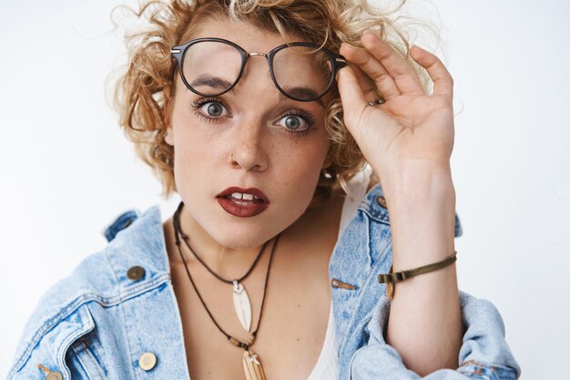 Closeup shot of surprised and impressed speechless attractive woman seeing incredible promotion taking off glasses popping eyes at front open mouth from amazement over white wall