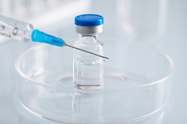 Closeup shot of a syringe and a closed glass vial with clear liquid in a glass dish at a lab