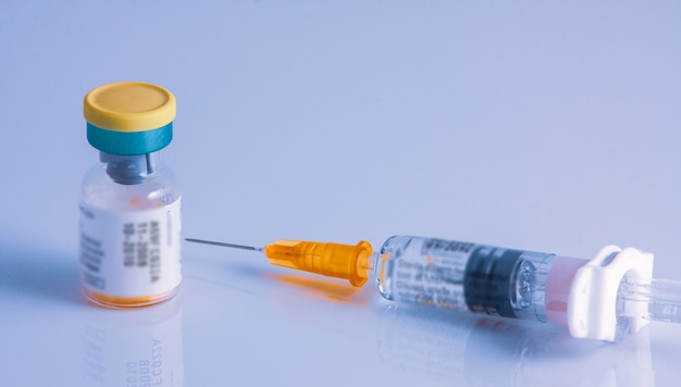 Closeup shot of a syringe a vial on a white glossy surface