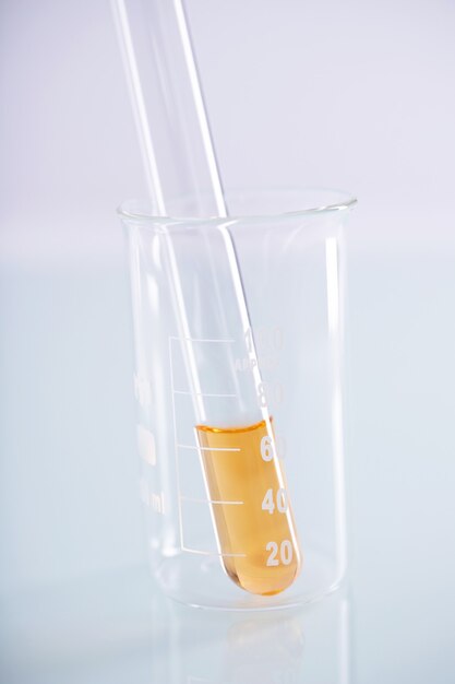 Closeup shot of a test tube with yellow liquid inside a beaker on a white surface