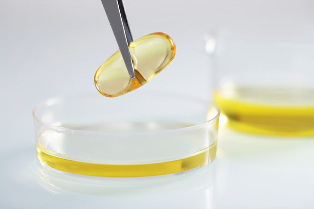 Free photo closeup shot of tweezers holding a clear yellow capsule over yellow liquid in a glass dish at a lab