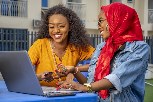 Closeup shot of two cheerful young African ladies and a laptop