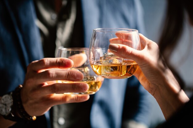 Closeup shot of two people clinking glasses with alcohol at a toast