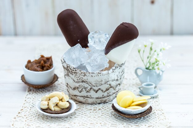 Closeup shot of vegan ice-cream on a stick in a bowl with ice cubes on a table with other snacks