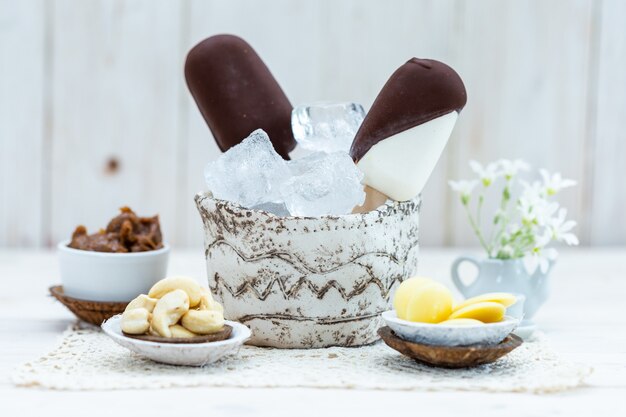 Closeup shot of vegan ice-cream on a stick in a bowl with ice cubes on a table with other snacks