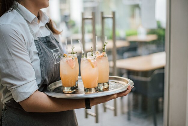 Closeup shot of a waiter serving cocktail with fresh oranges on a silver tray