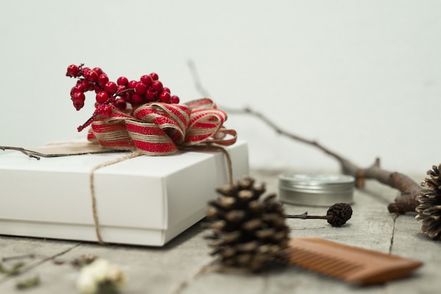 Closeup shot of a white christmas gift box with a red bow on top of it on the table near pine cones