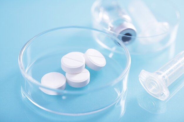 Closeup shot of  white pills in a glass dish at a lab